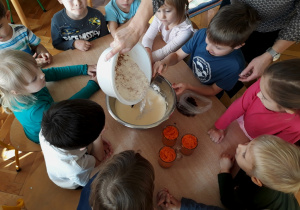 Nauczycielka wsypuje mąkę, chłopiec miesza ciasto.