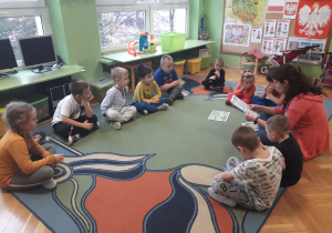 Dzieci siedzą w kole i słuchają opowiadania czytanego przez nauczycielkę