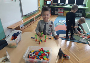 Chłopiec siedzi przy stoliku i pokazuje swoją budowlę