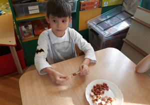 Chłopiec nakłada na patyczek cząstki sera, parówki, ogórka i kabanosa