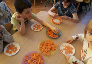 Dzieci robią obrazki z marchewki na talerzykach