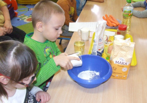 Chłopiec wsypuje mąkę do miski.