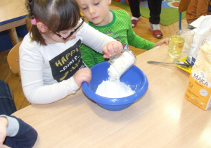 Dziewczynka wsypuje mąkę do miski.