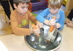 Chłopcy ścierają marchewkę na tarce.