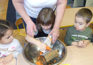 Dziewczynka ściera marchewkę na tarce.