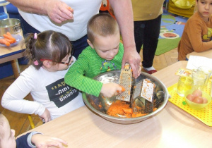 Chłopiec ściera marchewkę na tarce.