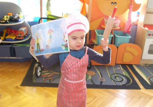 Chłopiec przebrany za kucharza trzyma ilustrację i wałek do ciasta.