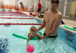 Dziecko pływa w basenie pod kierunkiem trenera
