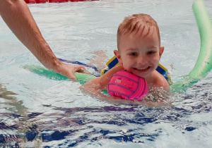 Dziecko pływa w basenie pod kierunkiem trenera