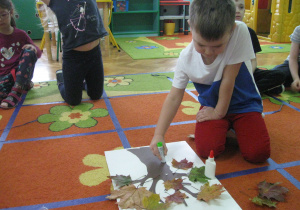 Chłopiec przykleja liść przy pomocy kleju.