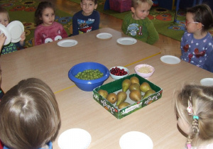 Dzieci siedzą przy stolikach oglądają owoce do jeżyków.