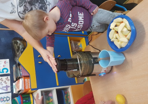 Chłopiec z pomocą nauczycielki wkłada jabłko do sokowirówki.