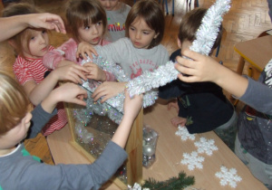 Dzieci wkładają łańcuch choinkowy do pojemnika.