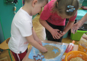 Dzieci wykrawają foremkami kształty ciasteczek.