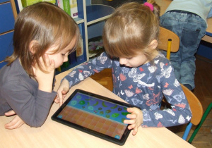 Dziewczynki wspólnie korzystają z aplikacji na tablecie.