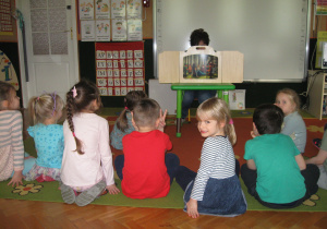 Dzieci siedzą. Oglądają trzeatrzyk Kamishibai.