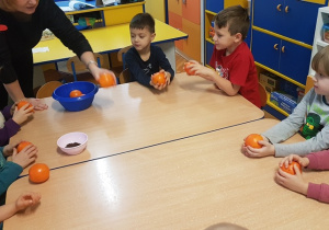 Nauczycielka rozdaje dzieciom pomarańcze.