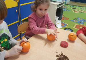 Dzieci ozdabiają pomarańczę.