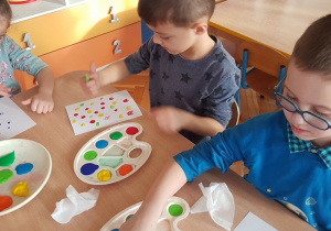 Dzieci przy stole odbijają na kartce kropki z farby palcem.