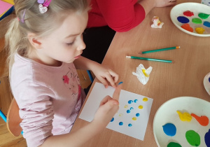 Dziewczynka robi kropeczki z farby na kartce palcem.