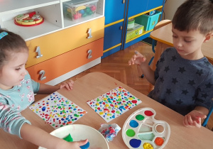 Dzieci przy stole odbijają na kartce kropki z farby palcem.