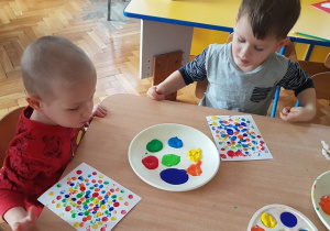 Chłopcy przy stole odbijają na kartce kropki z farby palcem.