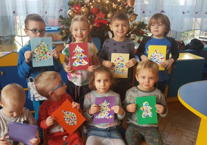 Dzieci przy choince z wykonanymi kartkami świątecznymi.