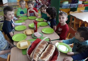 Dzieci siedzą przy stole, obserwują przygotowane składniki tostów.