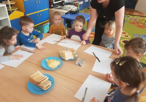 Dzieci siedzą przy stolikach ogladaja produkty do wykonania tostów.