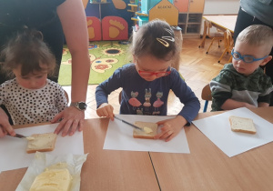 Dzieci smarują chleb tostowy masłem.