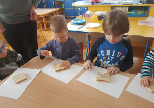 Dzieci smarują chleb tostowy masłem.