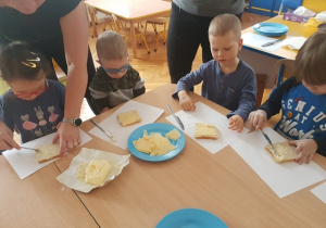 Dzieci smarują chleb tostowy masłem i układają ser.