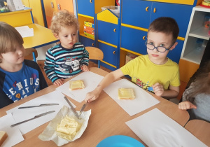 Dzieci smarują chleb tostowy masłem i układają ser.