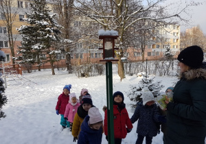 Nauczycielka w ogrodzie przedszkolnym pokazuje dzieciom karmnik dla ptaków