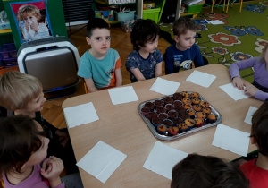 Dzieci siedzą przy stole, na środku stoi taca z muffinkami