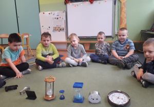 Dzieci siedzą na dywanie i oglądają zegary.
