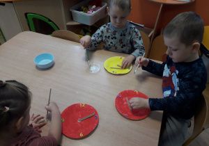 Dzieci siedzą przy stoliku i robią zegar.