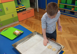 Chłopiec układa ciasteczka na blaszce do pieczenia.