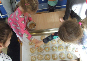 Dzieci posypują orzechami ciasteczka.