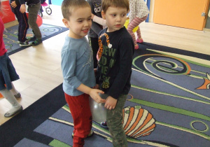 Dzieci tańczą w parach z balonikiem między kolanami.