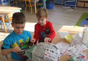 Chłopcy obklejają balon papierem.