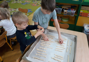 Dzieci układają paluszki z ciasta na brytfannie