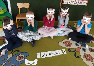 Dzieci prezentują maski, na dywanie ułożony napis "karnawał"