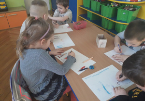 Dzieci siedzą przy stoliku i rysują swoją rodzinę.