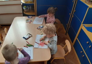 Dzieci przy stolikach kolorują obrazki.