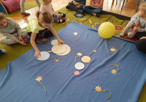 Na dywanie dzieci układają papierowy Układ Słoneczny.