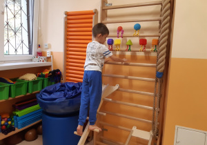 Chłopiec stojąc na przekładce ze szczebelkami układa sensoryczne kształty.
