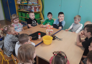 Dzieci siedzą przy stole, na którym stoją produkty potrzebne do zrobienia babeczek.