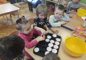 Dzieci wkładają do foremki papierowe papilotki do pieczenia babeczek.