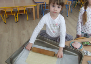 Dziewczynka wałkuje ciasto do pizzy.